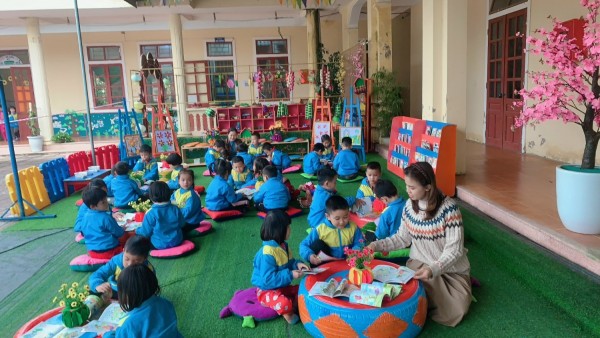 Cô Hiệu trưởng cùng trẻ 5 tuổi B xem sách ở góc Thư viện của bé