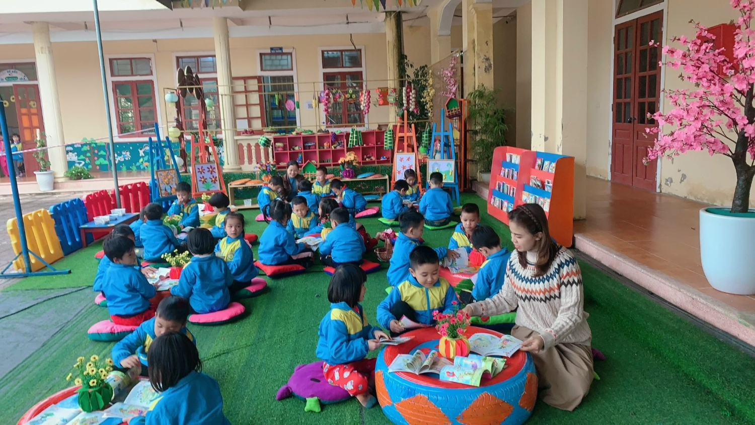 Cô Hiệu trưởng cùng trẻ 5 tuổi B xem sách ở góc Thư viện của bé